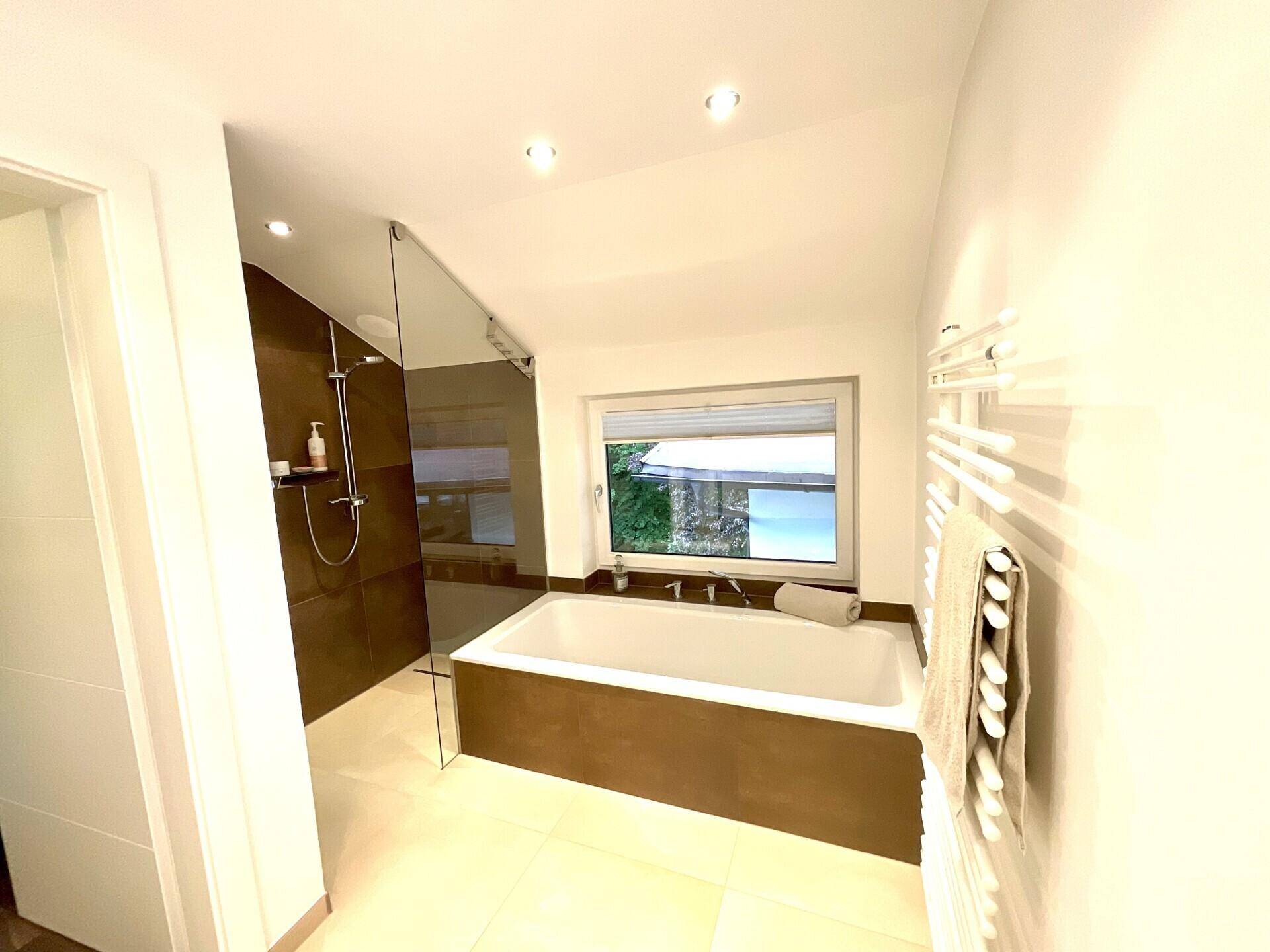 Modernes Badezimmer mit Badewanne, ebenerdiger Dusche und Fenster für natürliches Licht.