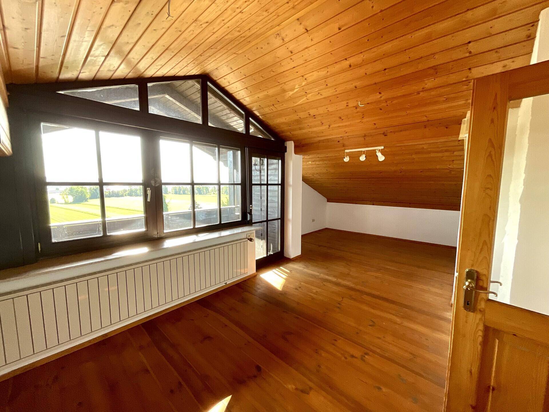 Gemütliches Zimmer im Dachgeschoss mit Holzvertäfelung, großen Fenstern und sonnigem Ausblick.