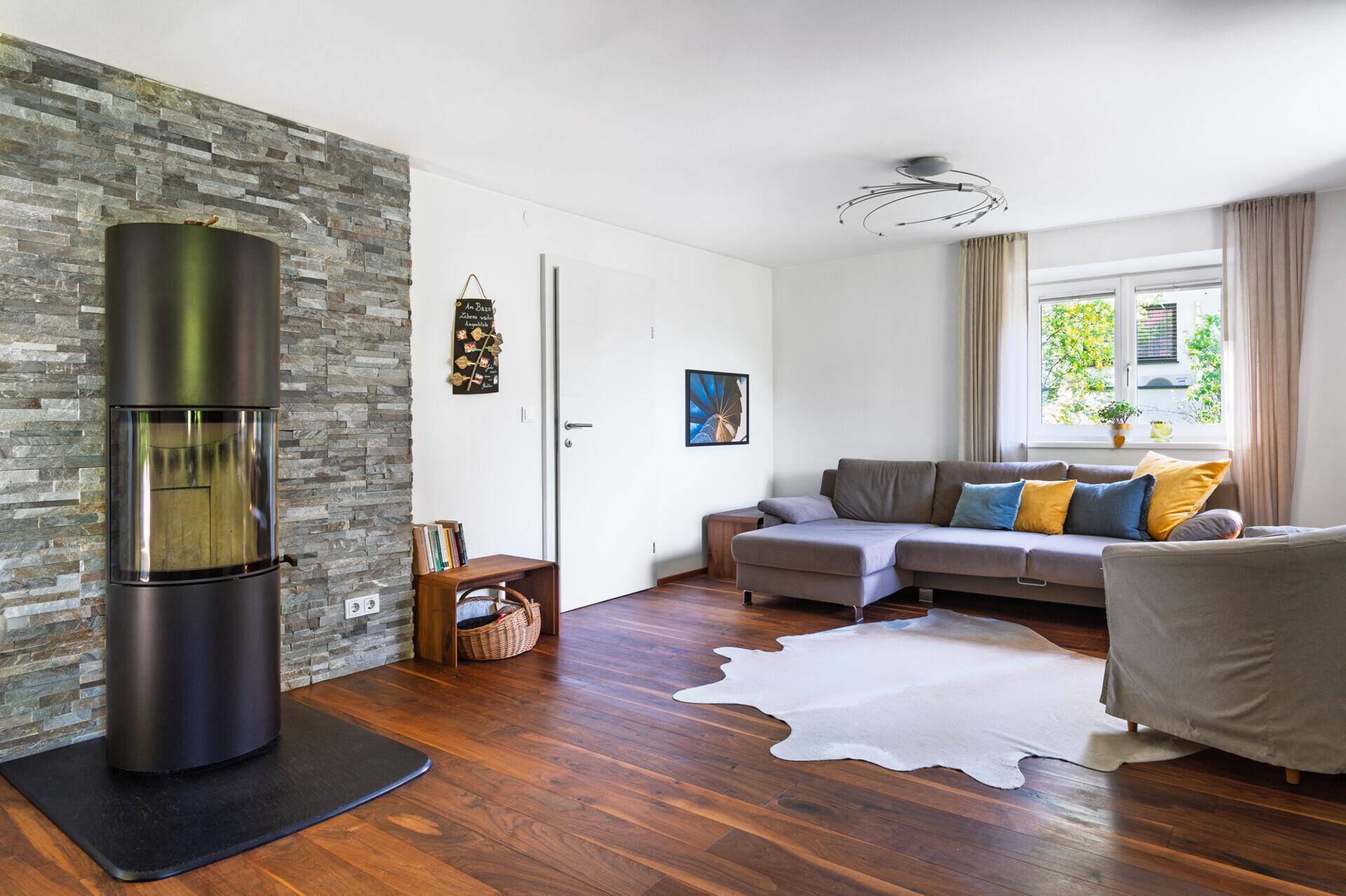 Helles Wohnzimmer mit modernem Kaminofen, Steinwand und gemütlichem Sofa, ideal zum Entspannen.