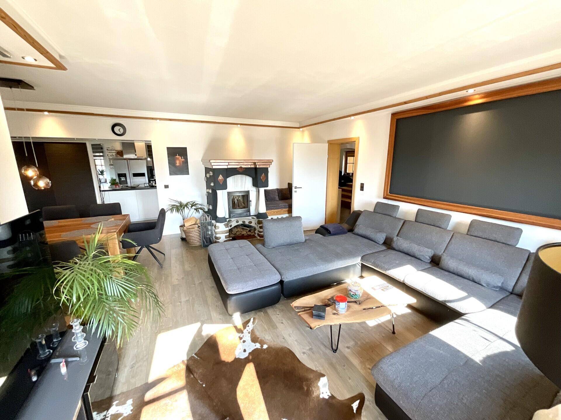 Helles, offenes Wohnzimmer mit großem Ecksofa, Kamin und Blick auf den Essbereich mit viel Tageslicht.