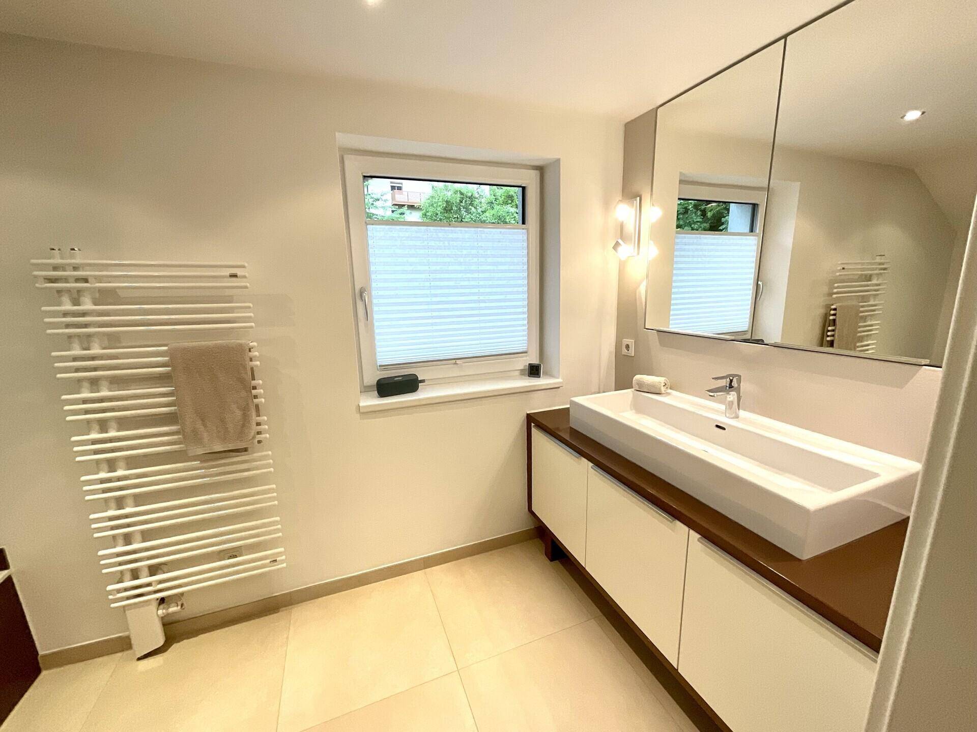 Helles Badezimmer mit modernem Waschtisch, Spiegelschrank und beheiztem Handtuchhalter.