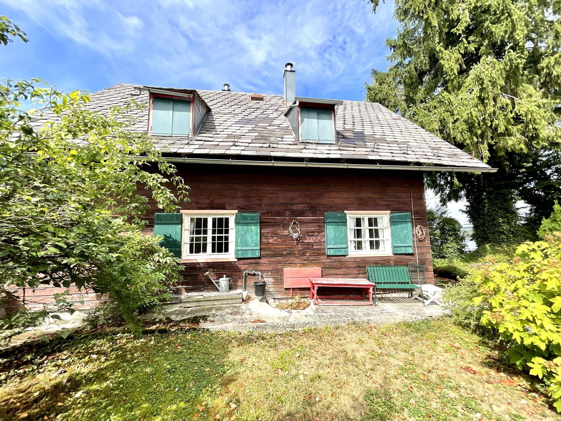 Charmantes Holzhaus mit traditionellen grünen Fensterläden und einem kleinen Gartenbereich vor der Fassade.