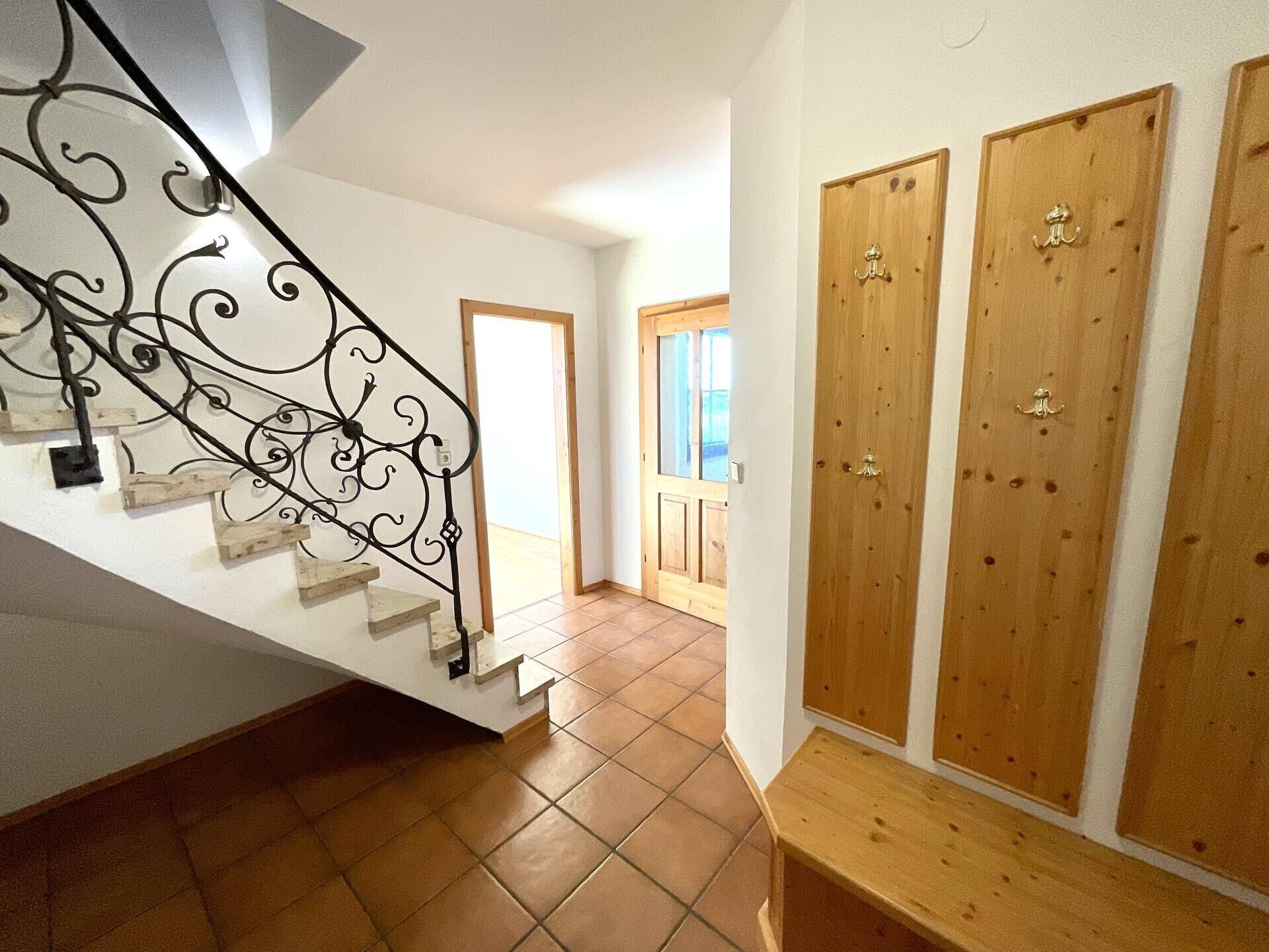 Heller Eingangsbereich mit Terrakottafliesen, Holzgarderobe und schmiedeeiserner Treppe.