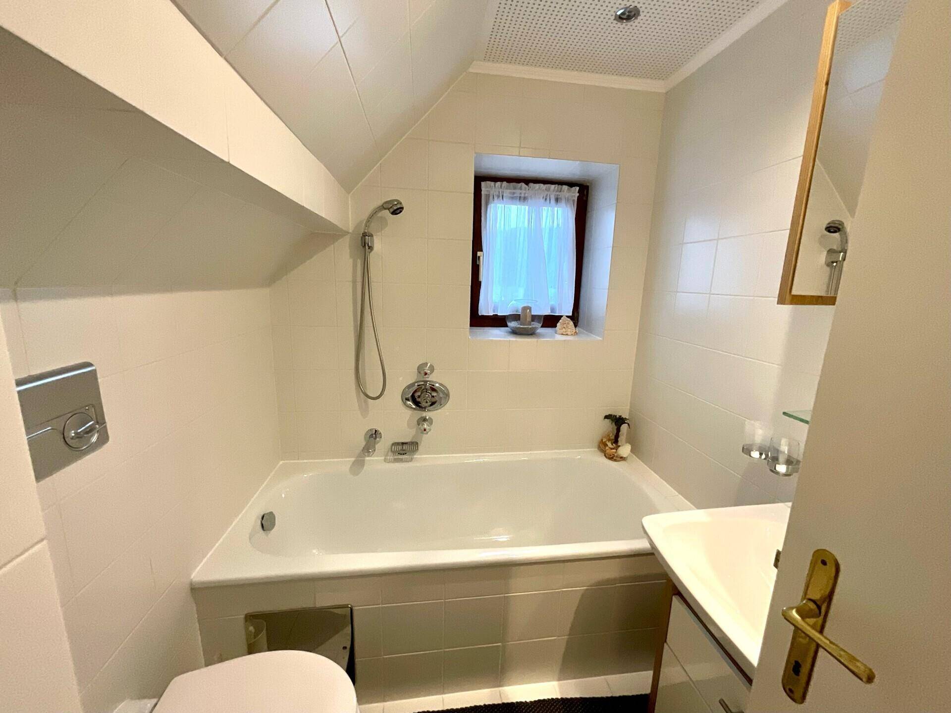 Helles Badezimmer mit Badewanne, WC und Fenster, das für natürliche Belüftung sorgt.