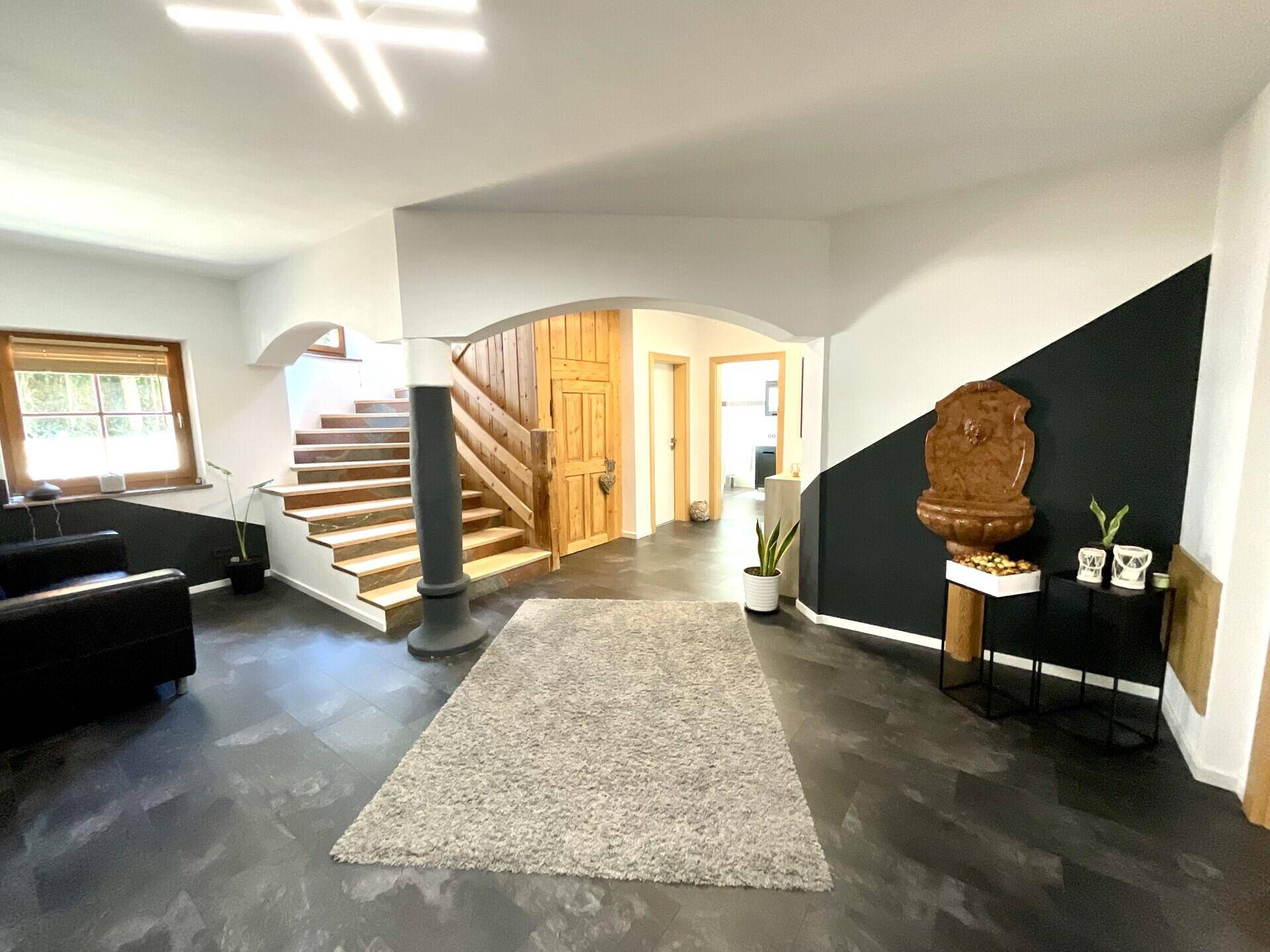 Heller Eingangsbereich mit Holztreppe, dunklem Boden und dekorativem Wandbrunnen in modernem Design.