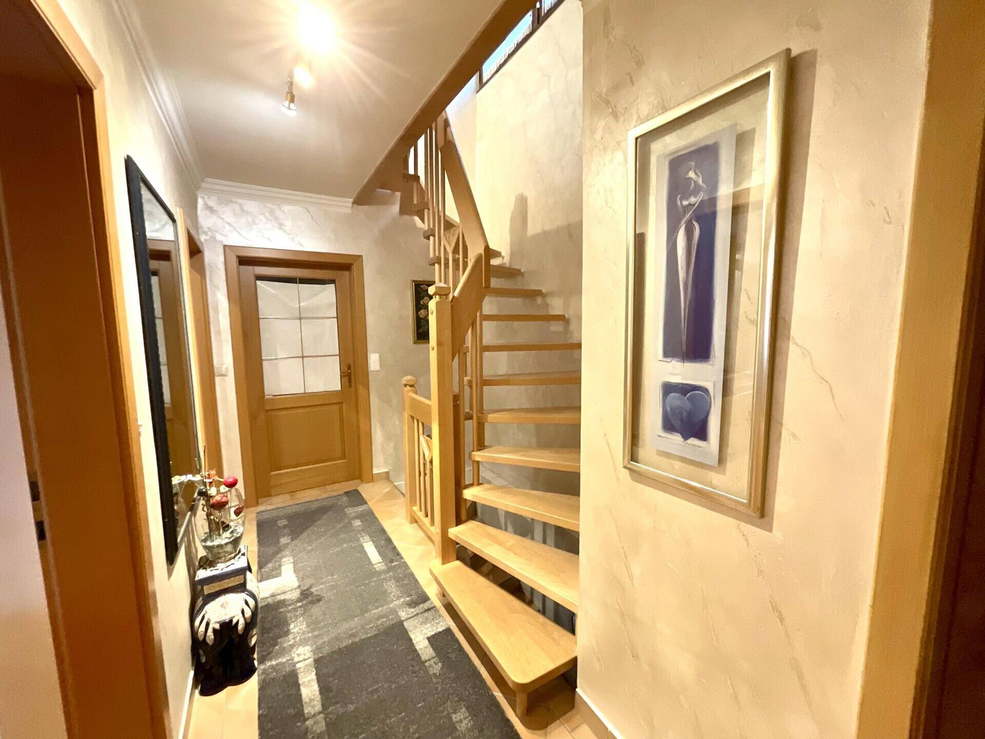 Geräumiger Flur mit heller Holztreppe und dekorativer Wandgestaltung, der die Etagen verbindet.