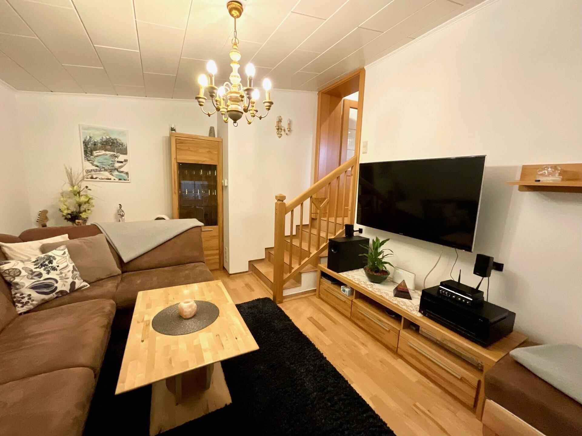 Gemütliches Wohnzimmer mit bequemer Couch, Holzboden und Fernseher, ideal zum Entspannen.
