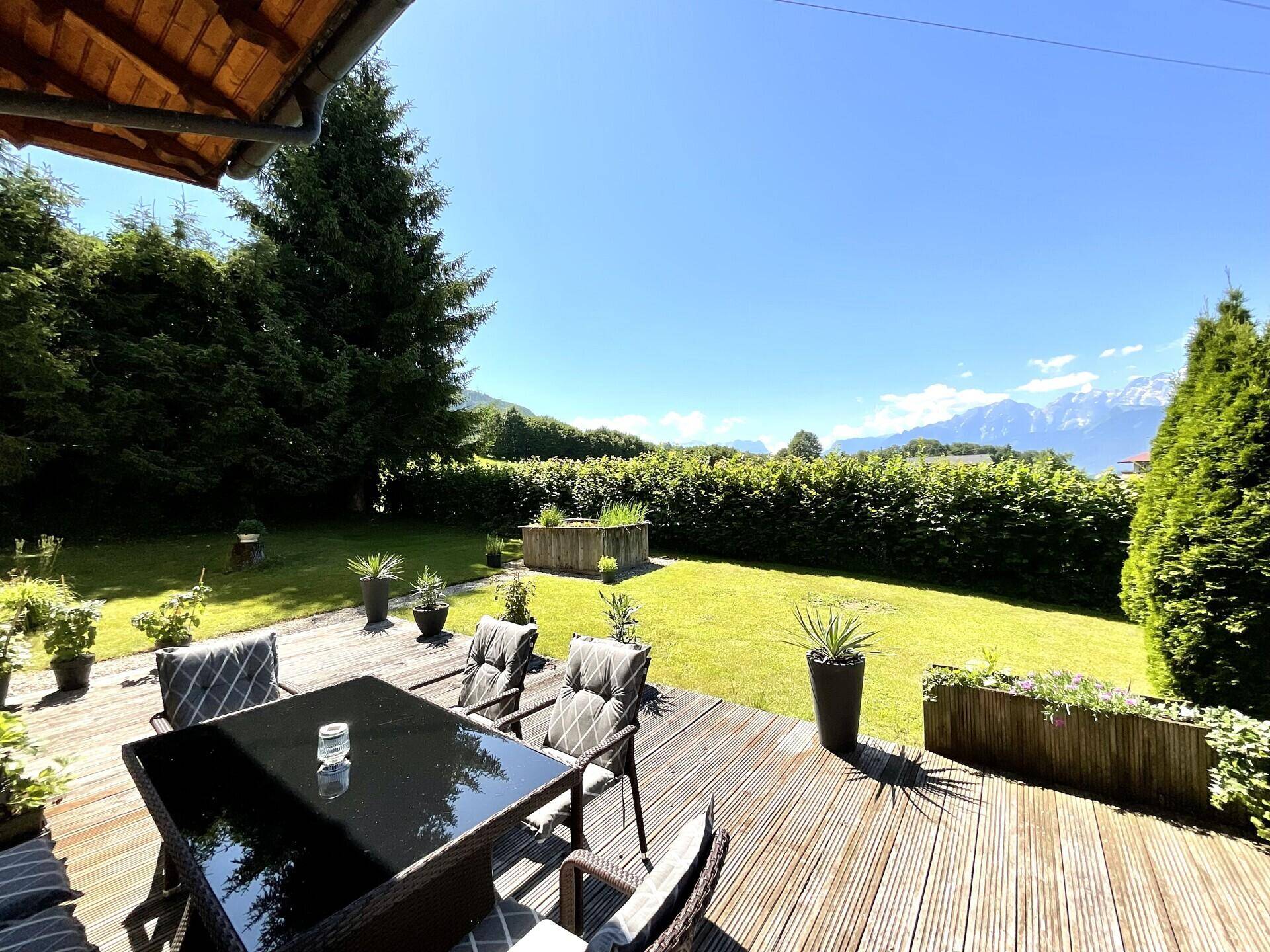 Geräumige Holzterrasse mit Esstisch und Stühlen, umgeben von einem gepflegten Garten und Bergblick.