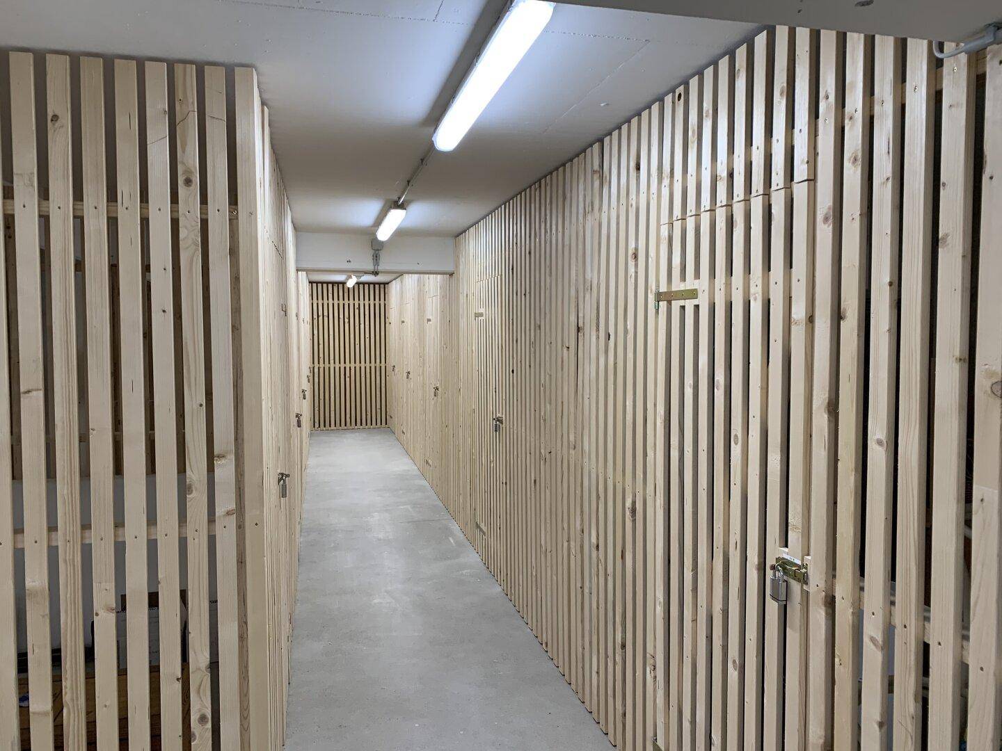 Langer Flur mit individuellen Lagerräumen, die durch Holzlattenwände abgetrennt sind.