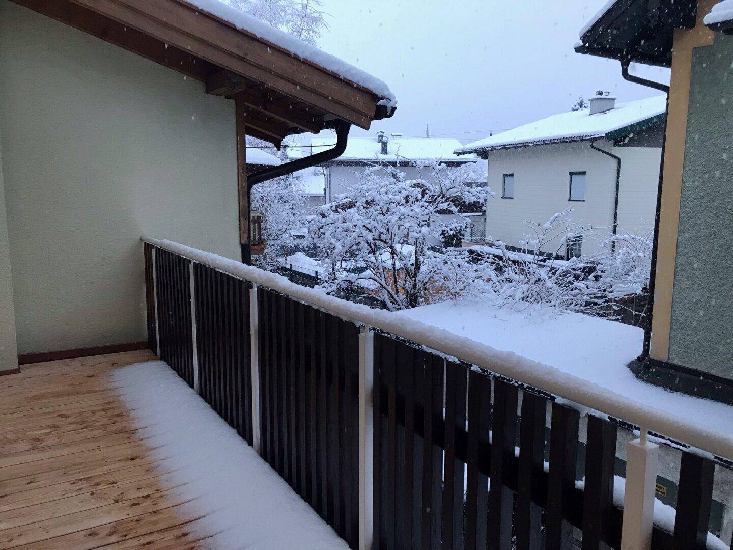 Balkon mit Holzbelag und Schneedecke, bietet einen Blick auf die verschneite Nachbarschaft.
