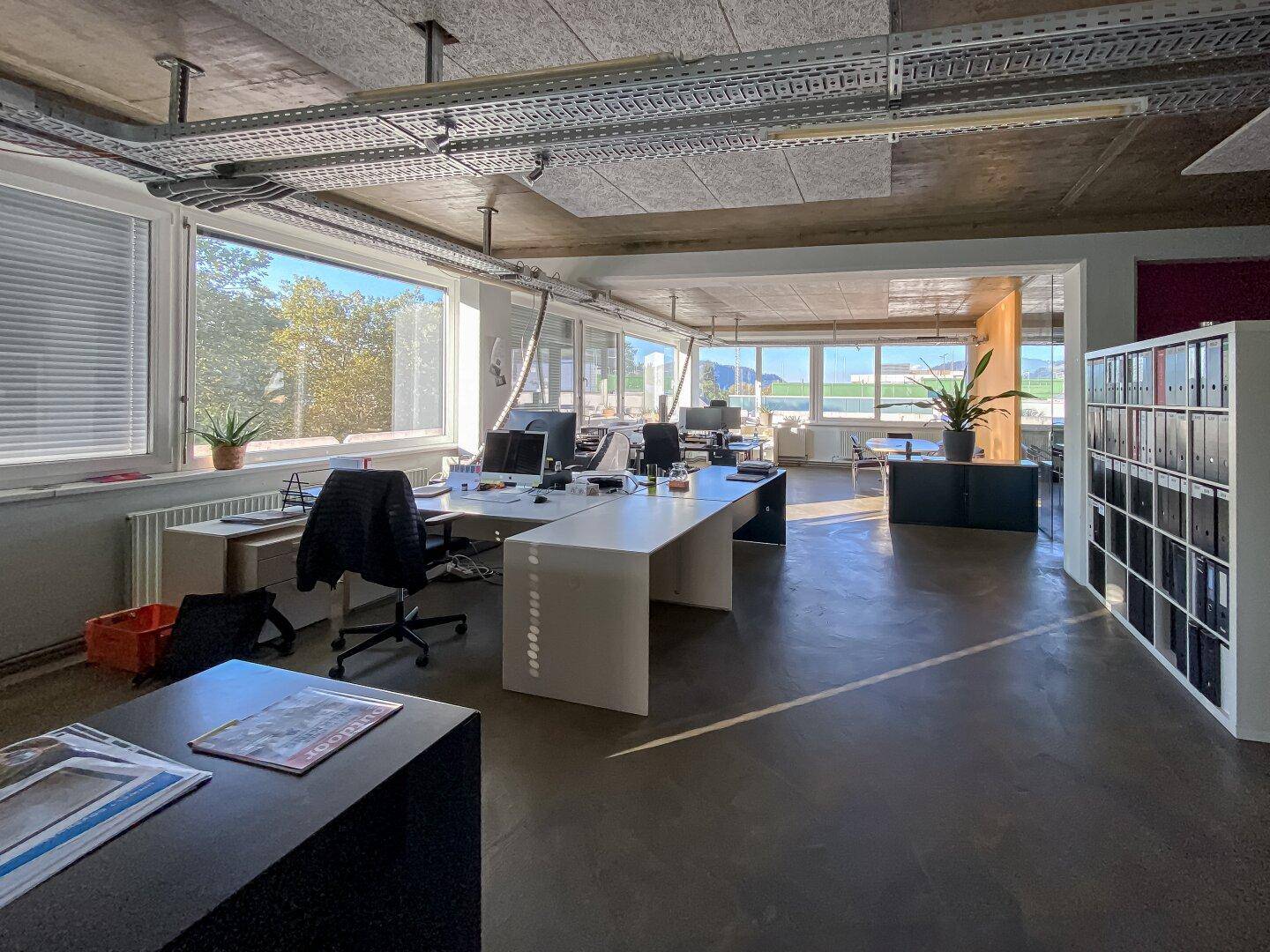 Helles Großraumbüro mit modernen Arbeitsplätzen, Betonboden und weitem Ausblick.