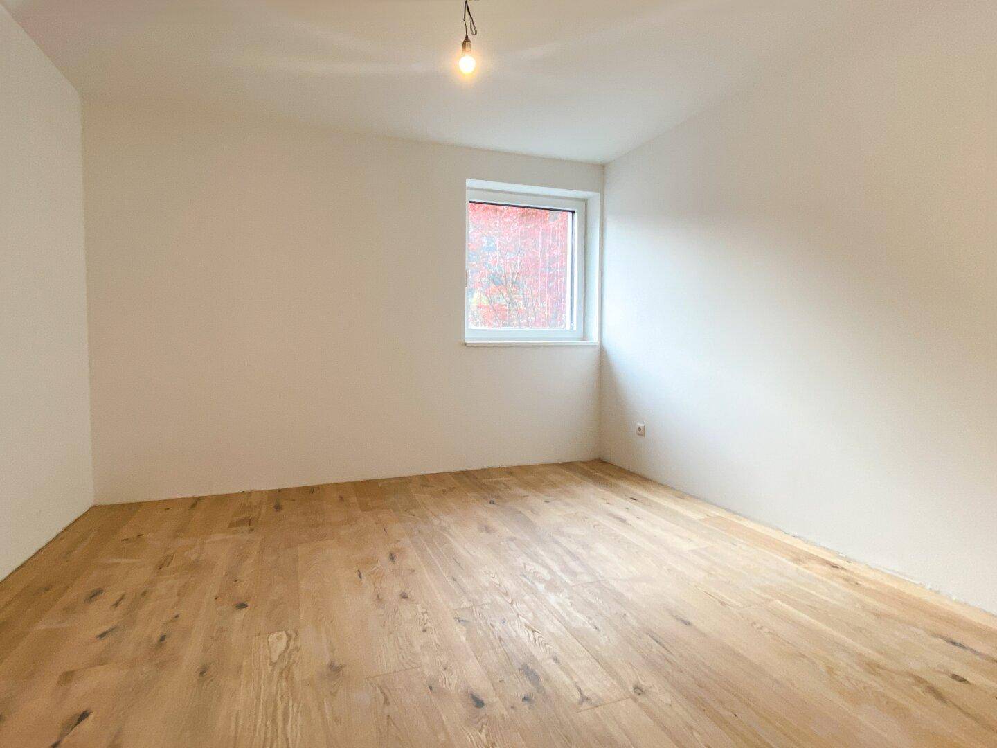 Helles Schlafzimmer mit neuem Holzparkett und einem Fenster, das viel Tageslicht hereinlässt.