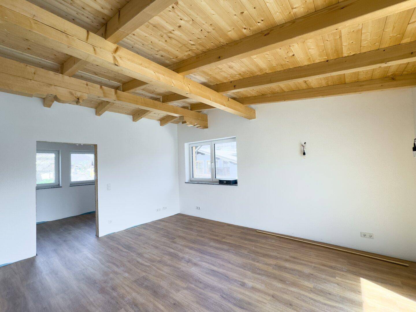 Heller Wohnraum mit Laminatboden, weißen Wänden und charakteristischen Holzdeckenbalken.