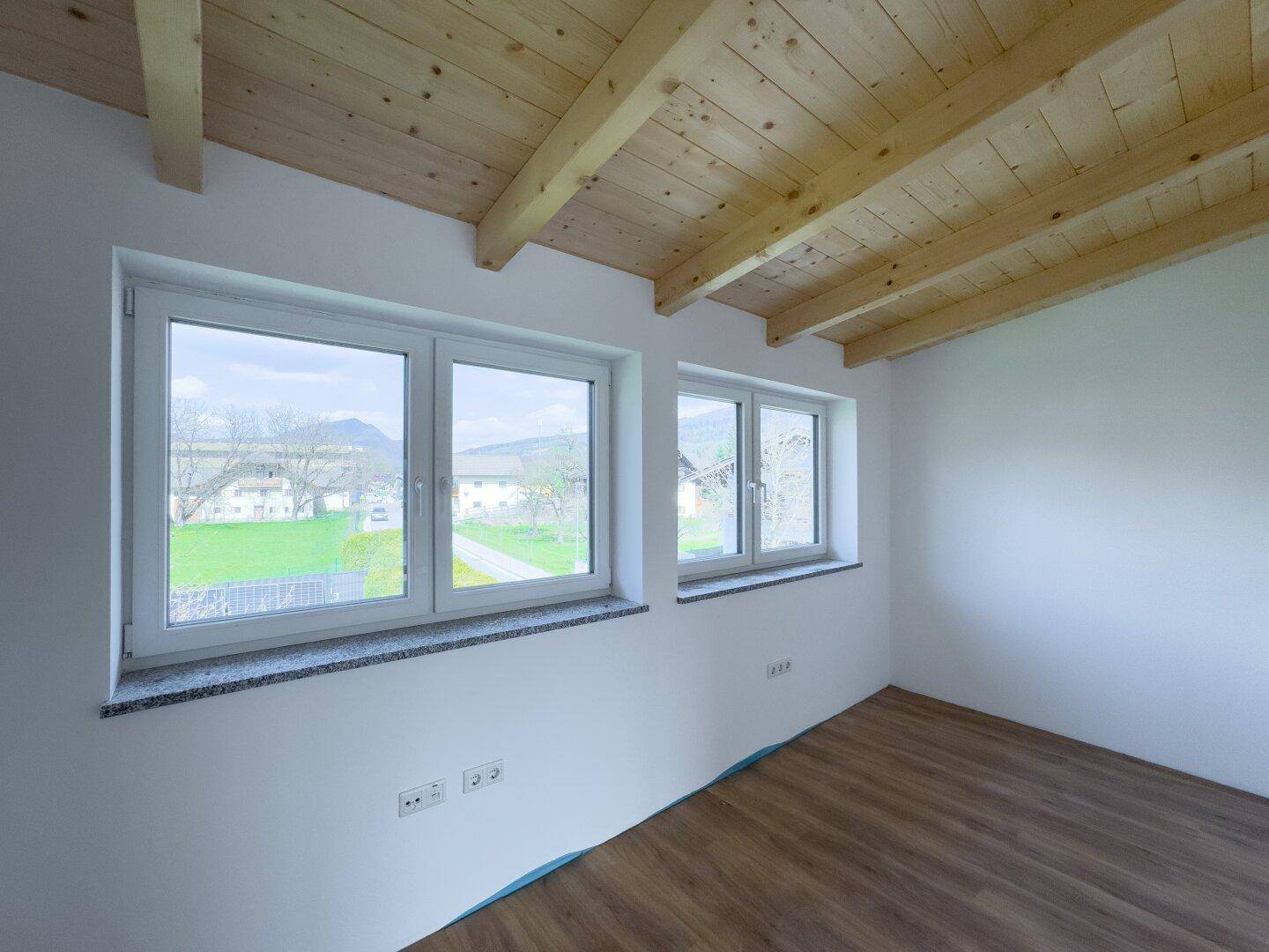 Helles Schlafzimmer mit Laminatboden, grüner Aussicht und rustikalen Holzdeckenbalken.