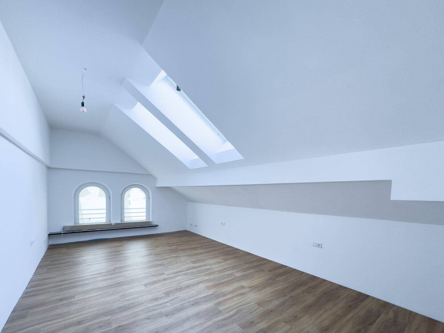 Geräumiger Dachbodenraum mit schrägen Decken, Dachfenstern und Rundbogenfenstern für viel Licht.