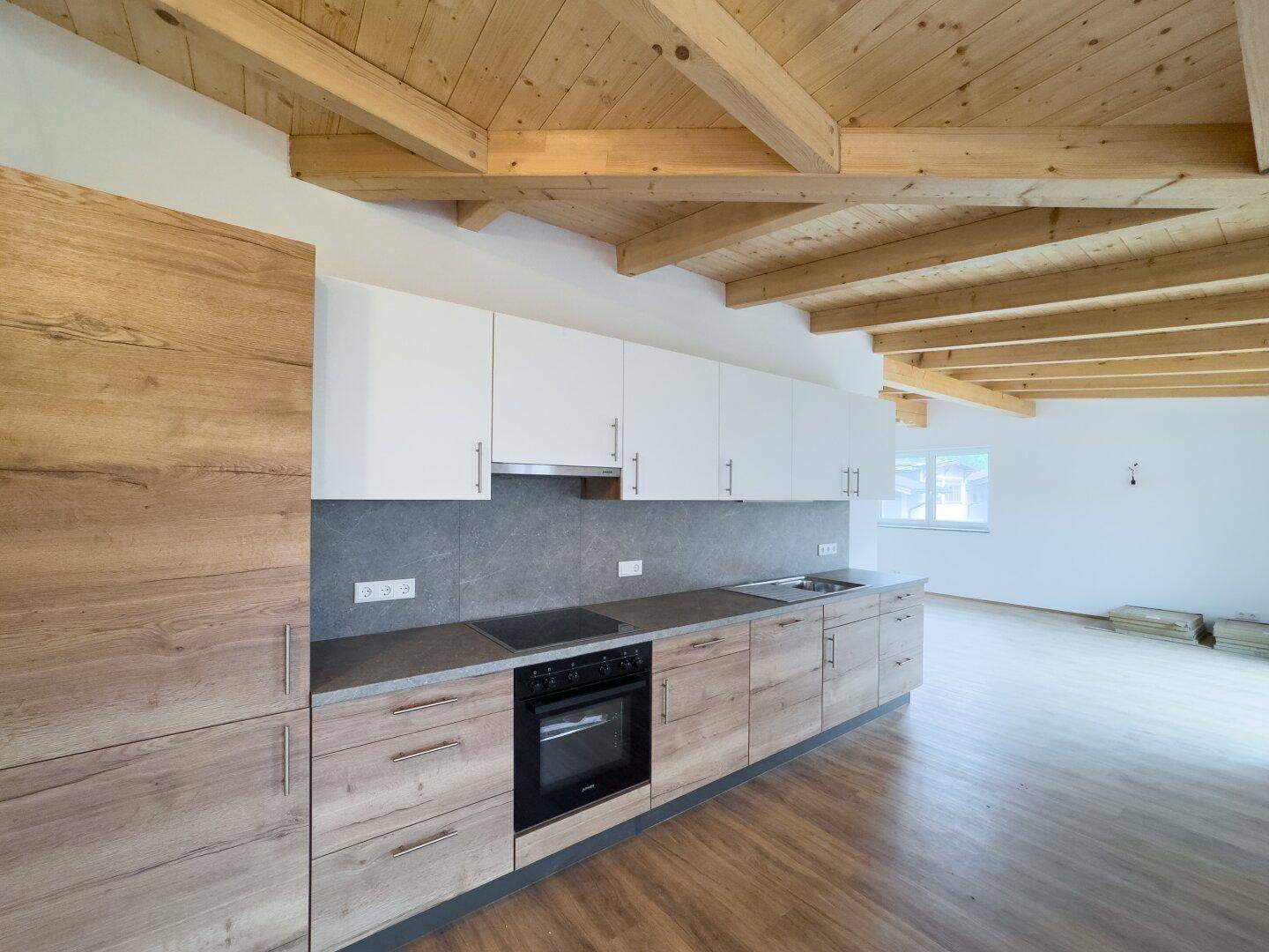 Moderne Einbauküche mit hellen Holzfronten, weißen Oberschränken und sichtbaren Holzdeckenbalken.