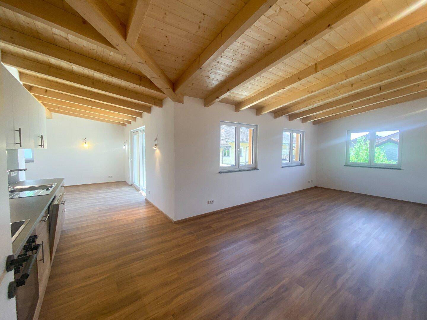 Offener Wohn- und Essbereich mit Laminatboden, sichtbaren Holzdeckenbalken und viel Tageslicht.