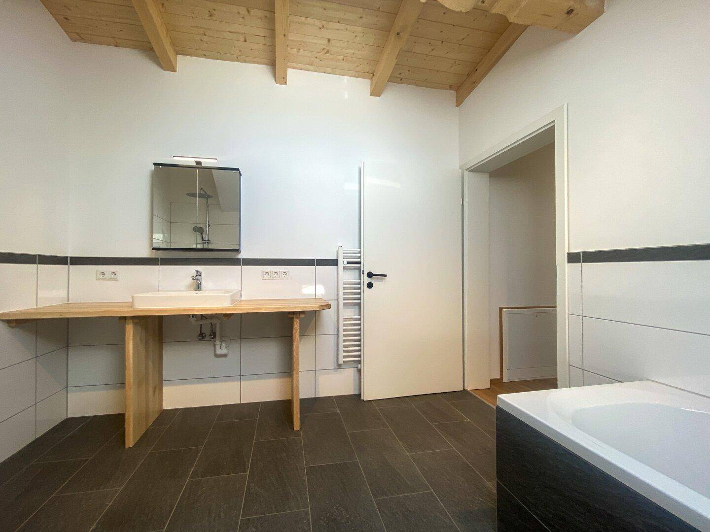Modernes Badezimmer mit dunklen Bodenfliesen, Badewanne, Einzelwaschbecken und Handtuchheizkörper.