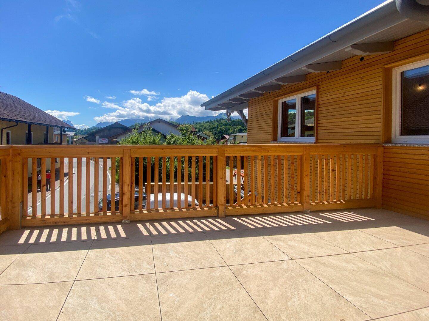 Geräumiger Balkon mit Fliesenboden, Holzgeländer und malerischem Bergblick unter blauem Himmel.