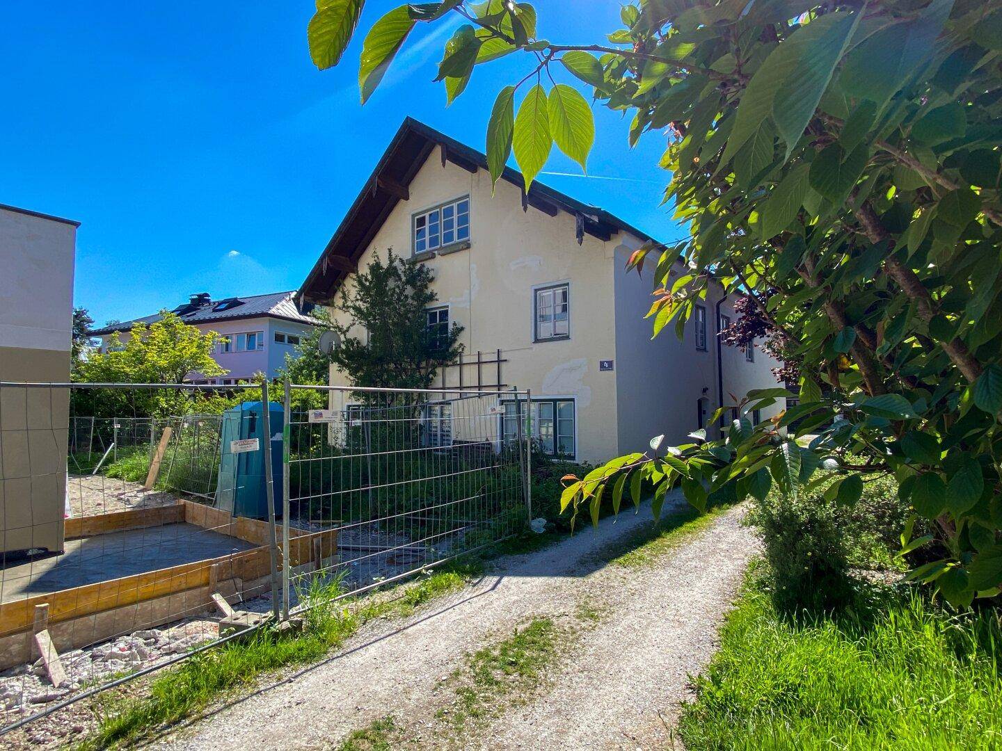 Hausansicht von der Zufahrt, mit angrenzender Baustelle und umgebendem Grün.