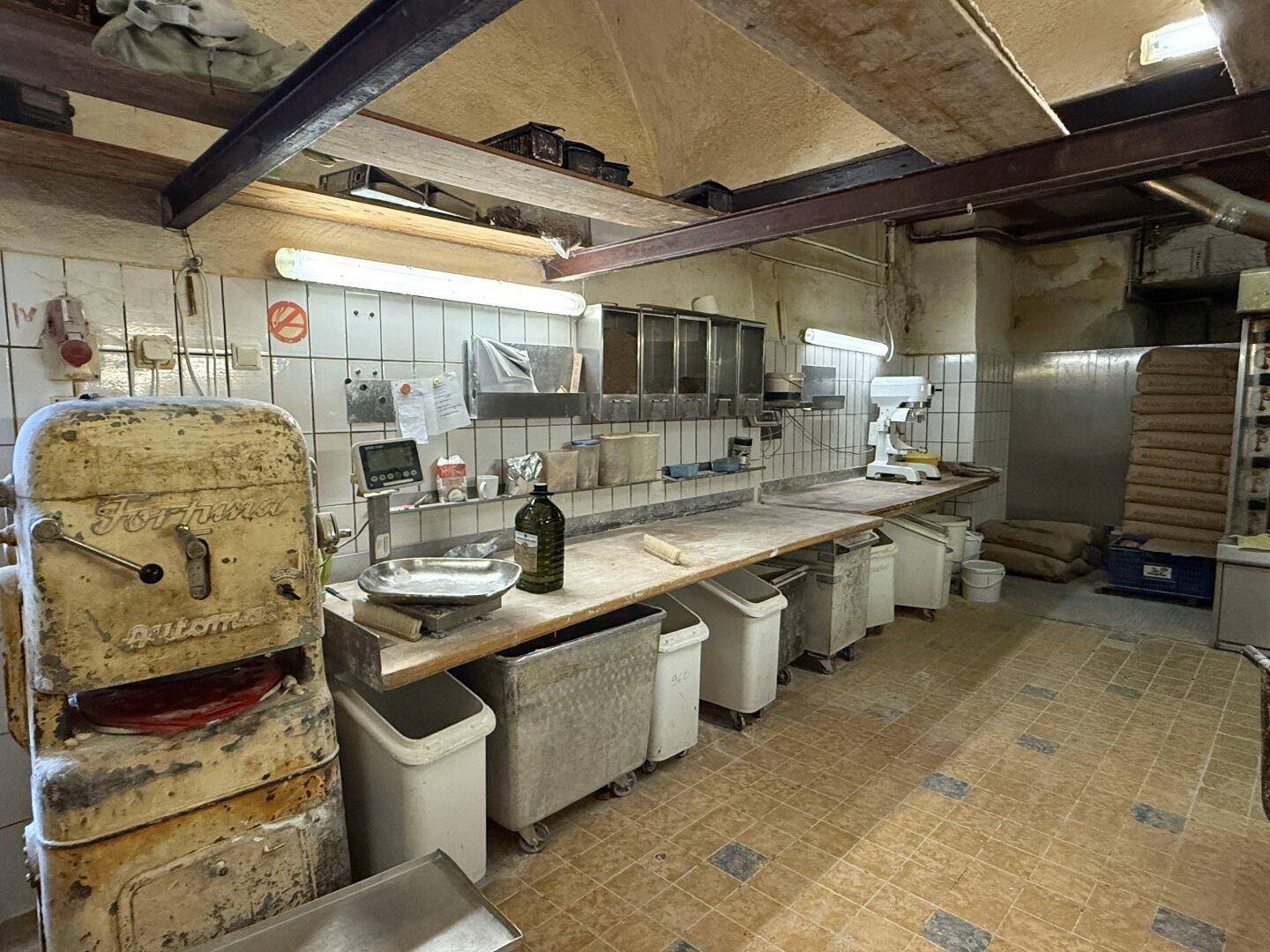 Detailansicht der Bäckereiküche mit alten Maschinen, gefliesten Wänden und robusten Arbeitsflächen.