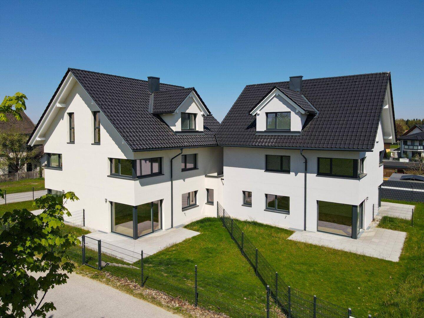 Zwei moderne Doppelhaushälften mit weißer Fassade und dunklem Satteldach in sonniger Lage.