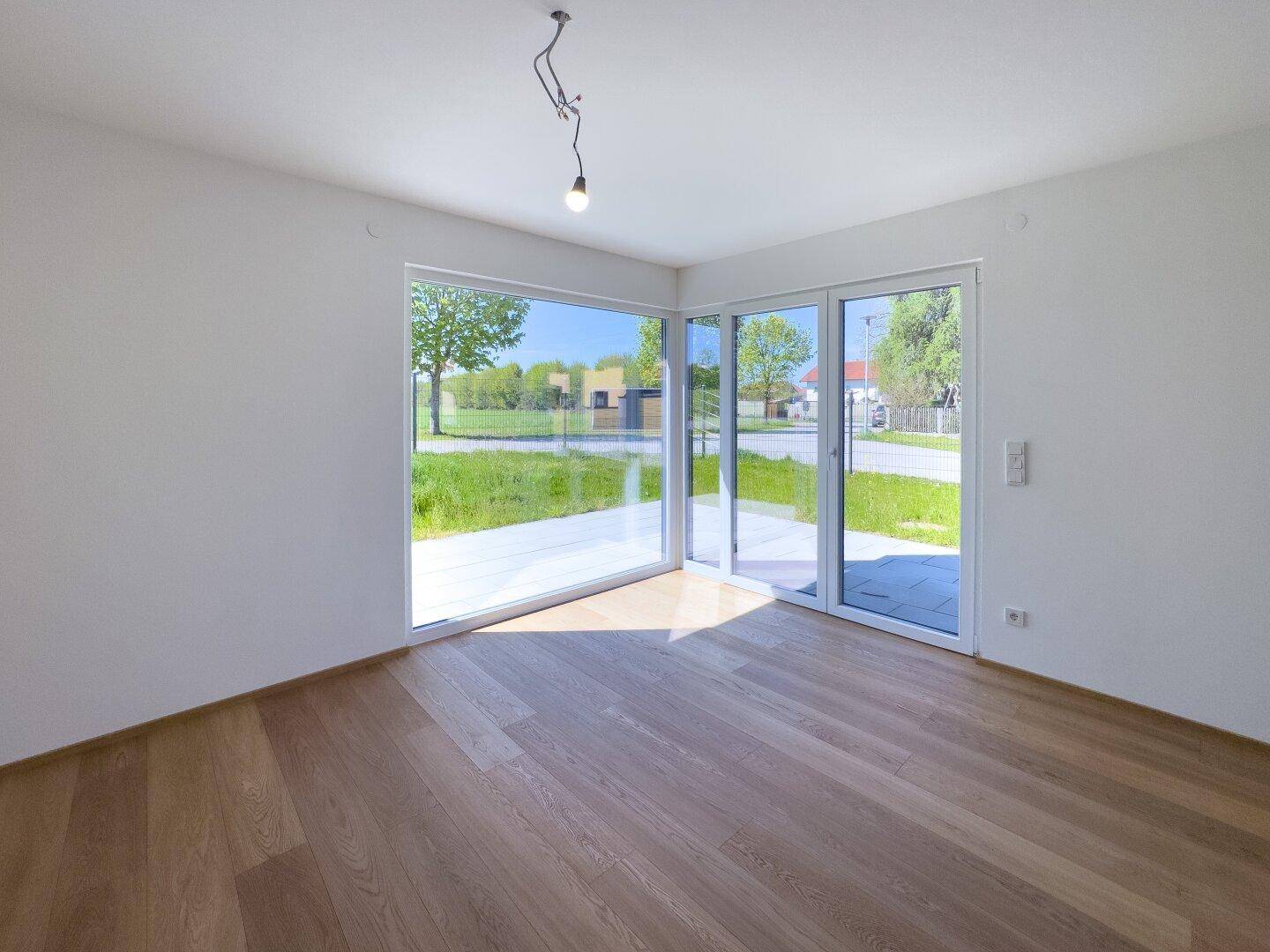 Heller Wohnbereich mit großen Fenstern, Holzboden und Zugang zur Terrasse mit Blick ins Grüne.