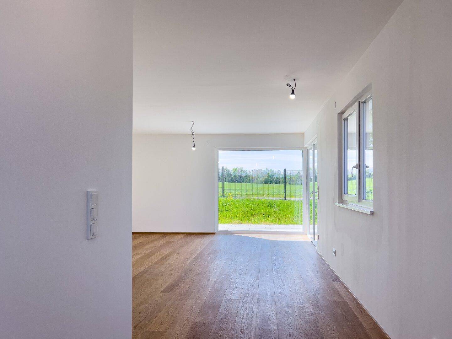 Lichtdurchfluteter Raum mit Holzboden und weitem Blick über die grüne Landschaft.