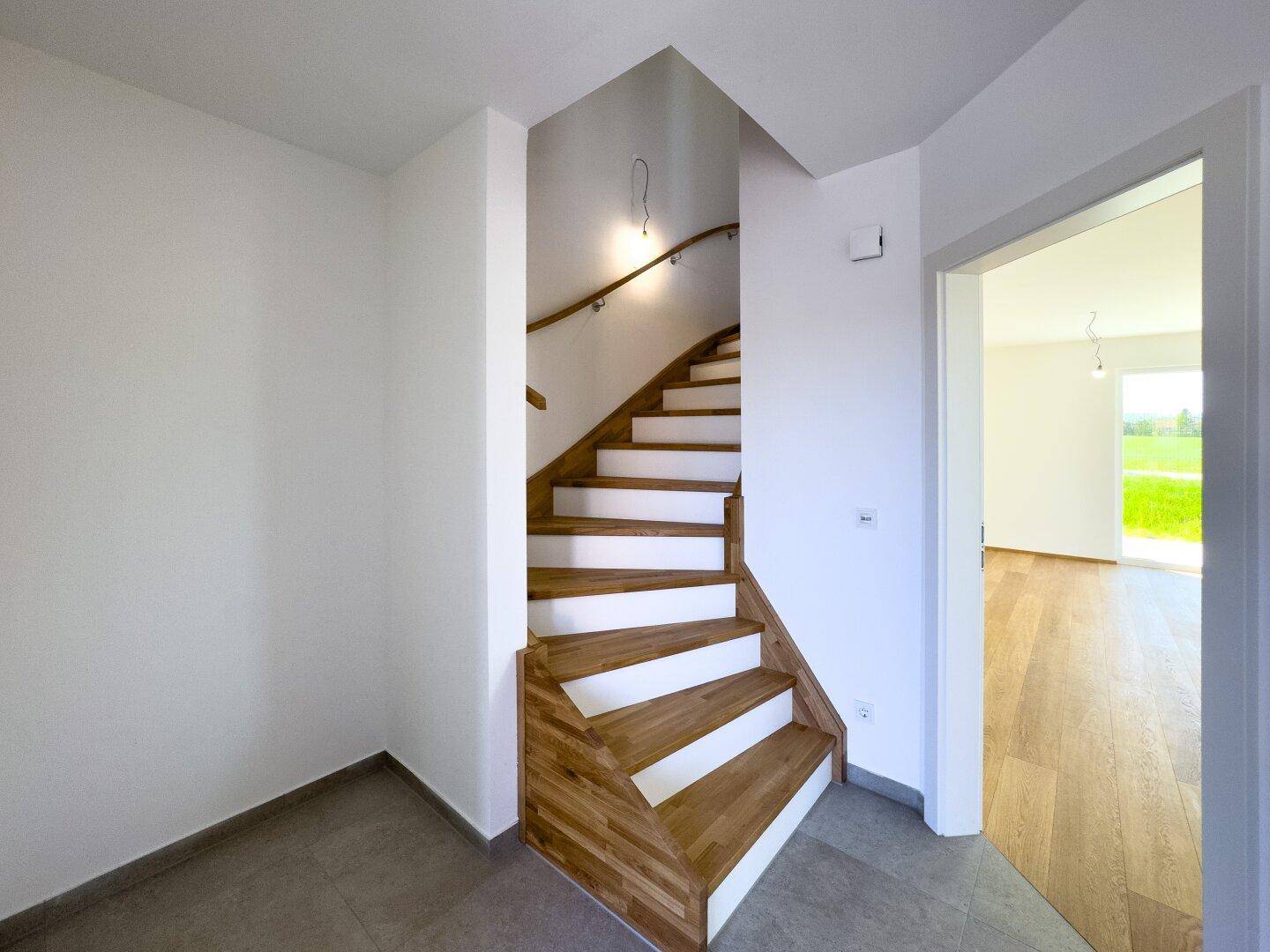 Heller Eingangsbereich mit Holztreppe und Fliesenboden, der zu den oberen Etagen führt.
