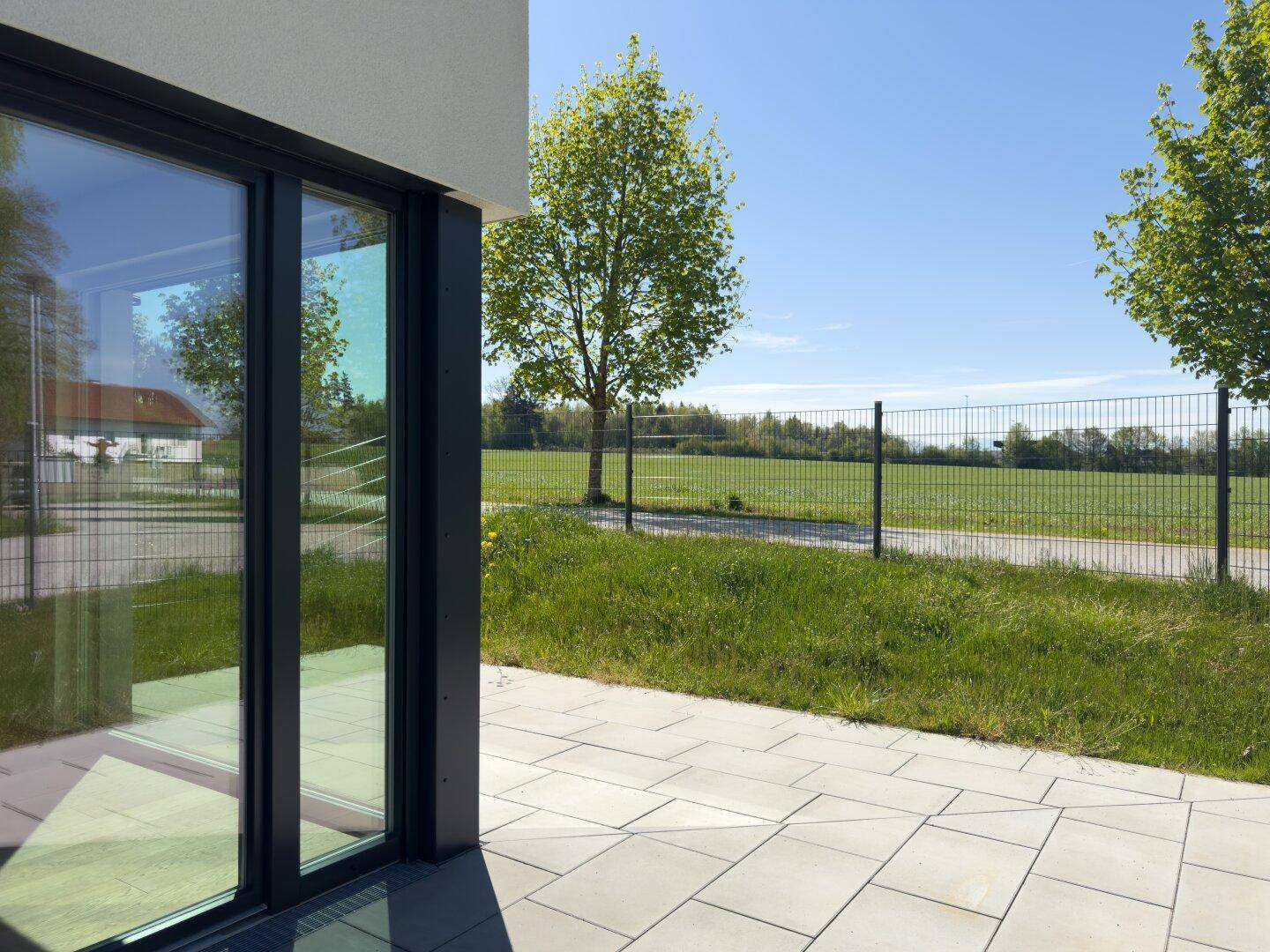 Gepflasterte Terrasse mit großen Glasfronten und direktem Zugang zum Garten mit Weitblick.