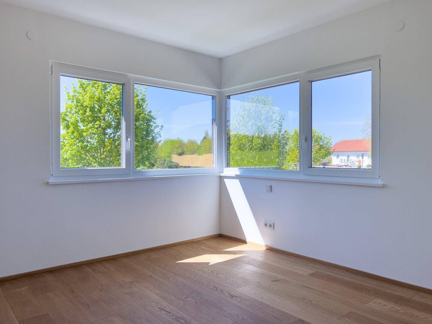 Helles Zimmer mit Holzboden und großen Fenstern, die viel Tageslicht hereinlassen.