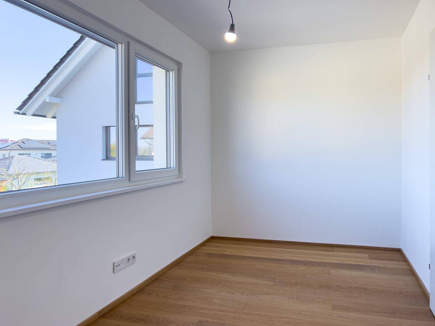Schlafzimmer mit Holzboden und Fenster, das einen Blick auf die Nachbarbebauung bietet.