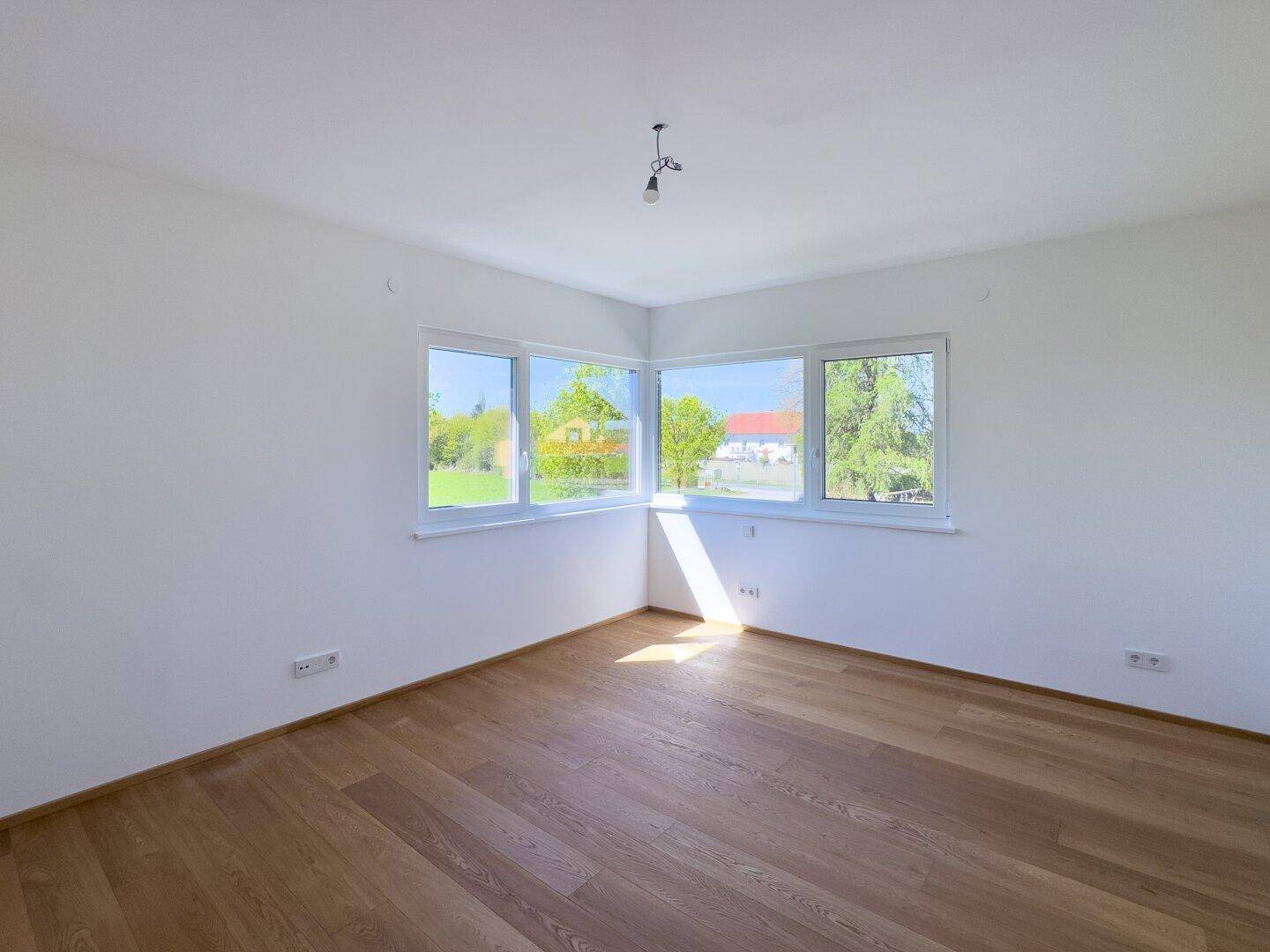 Helles Zimmer mit Holzboden und großen Fenstern, die viel Tageslicht hereinlassen.