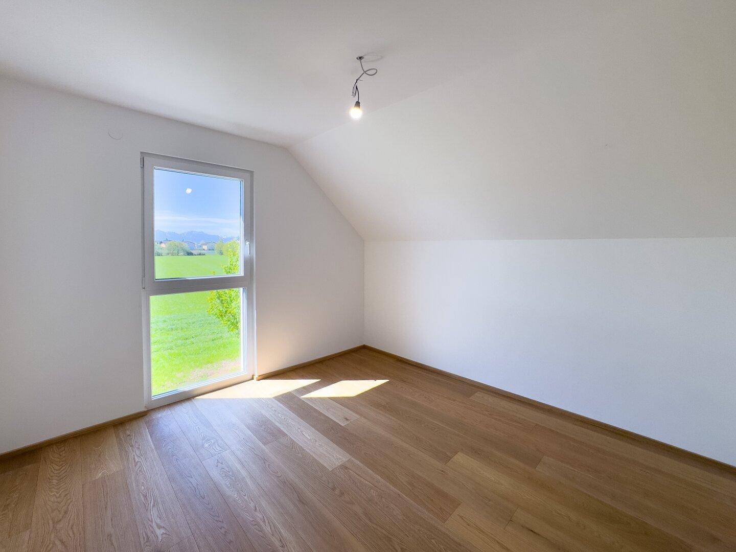 Dachgeschosszimmer mit Holzboden, schräger Decke und Fenster mit Bergblick.