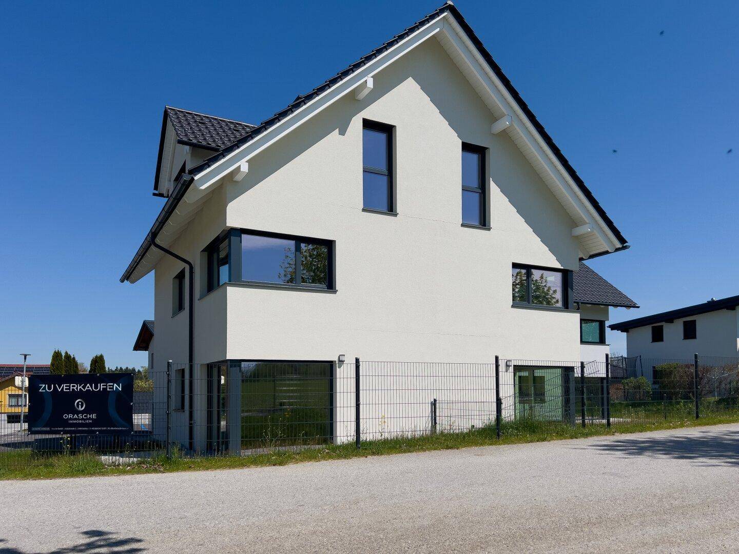 Seitenansicht einer modernen Doppelhaushälfte mit Verkaufsanzeige und Zaun.
