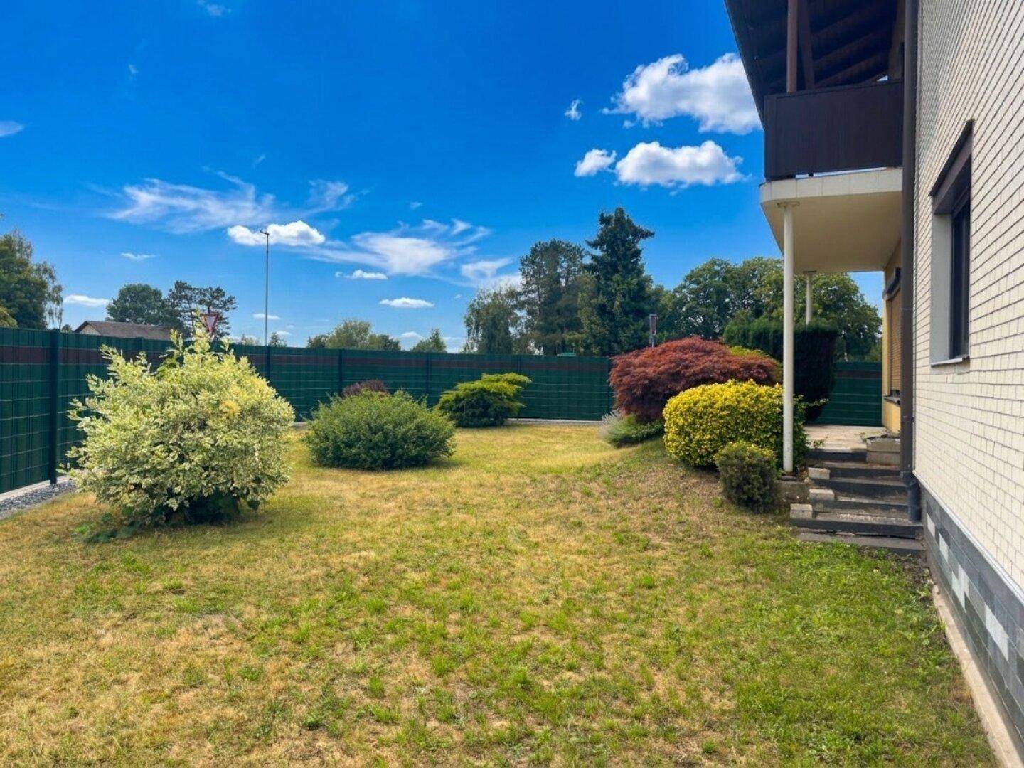 Gepflegter Gartenbereich mit Rasenfläche und Sträuchern, umgeben von einem Zaun.