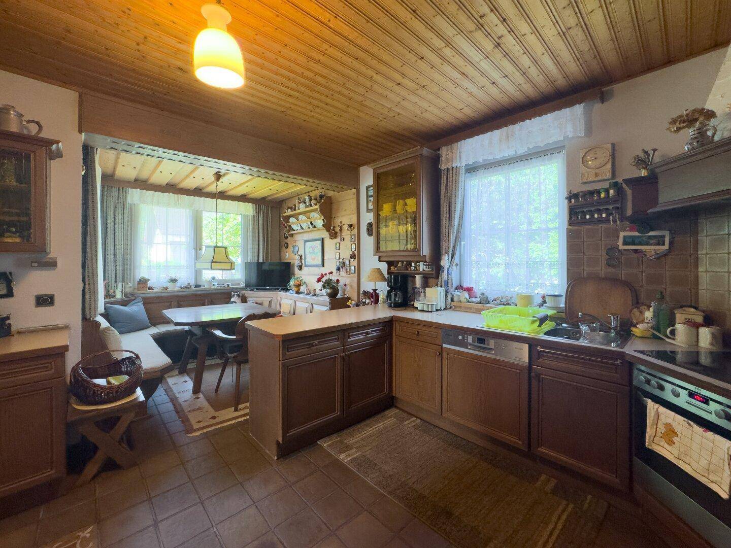 Traditionelle Wohnküche mit Holzdecken, Einbauküche und gemütlichem Essbereich am Fenster.