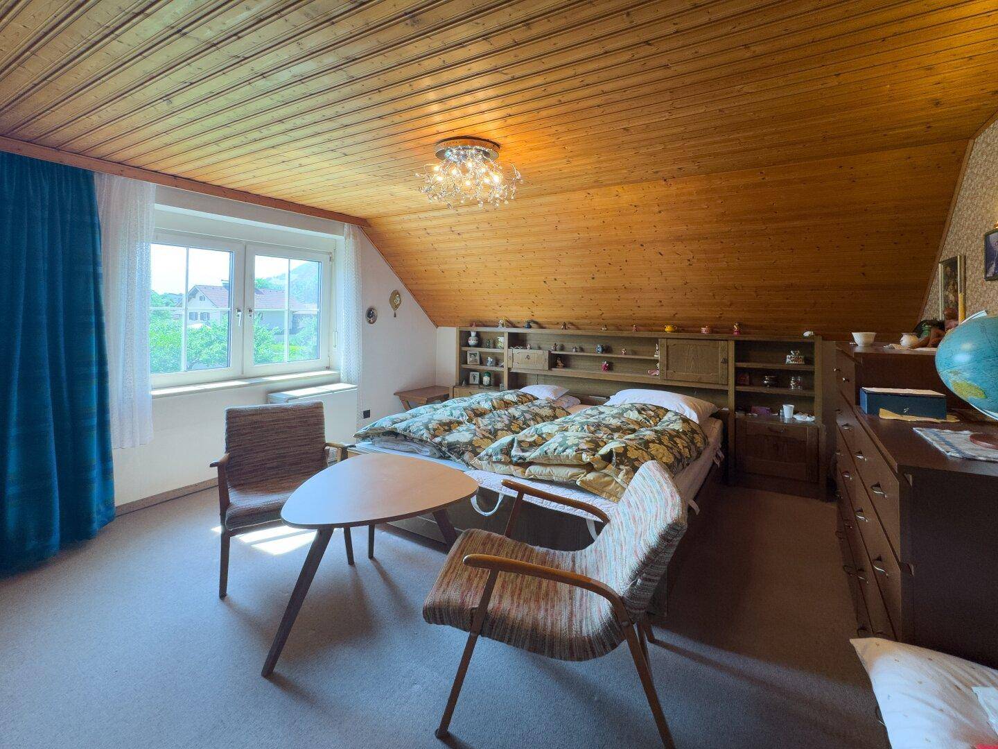 Schlafzimmer mit Dachschräge, Holzdecke, Teppichboden und Blick ins Grüne.