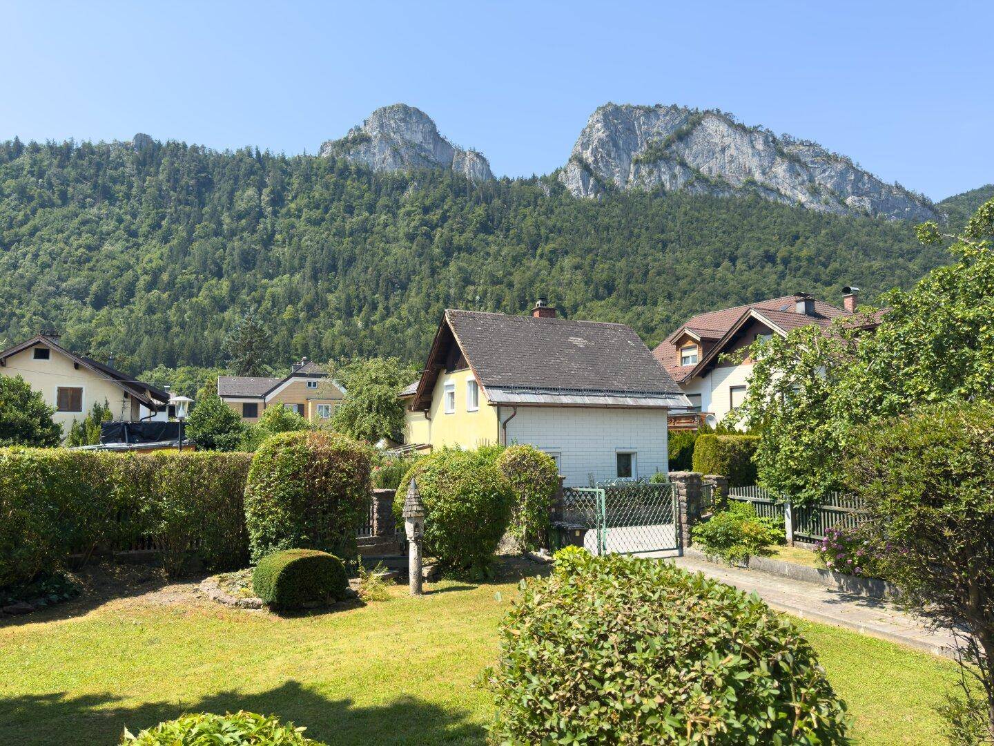 Haus mit gepflegtem Garten und beeindruckendem Bergblick im Hintergrund.
