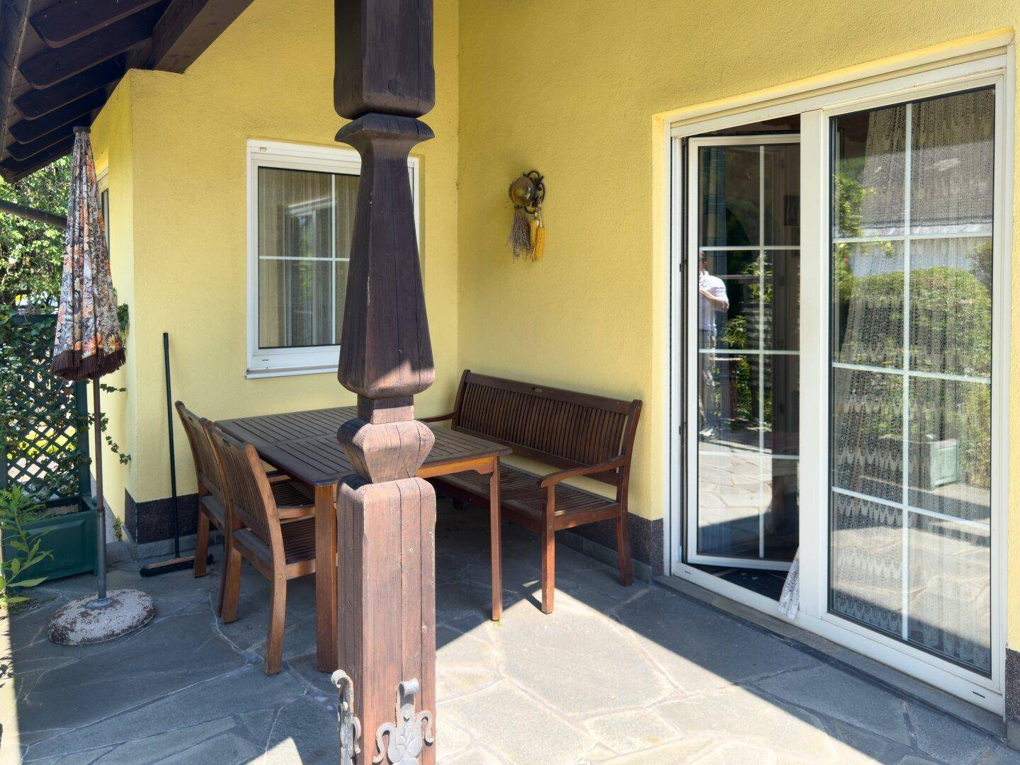 Überdachte Terrasse mit Holztisch und Sitzgelegenheiten, ideal für Mahlzeiten im Freien.