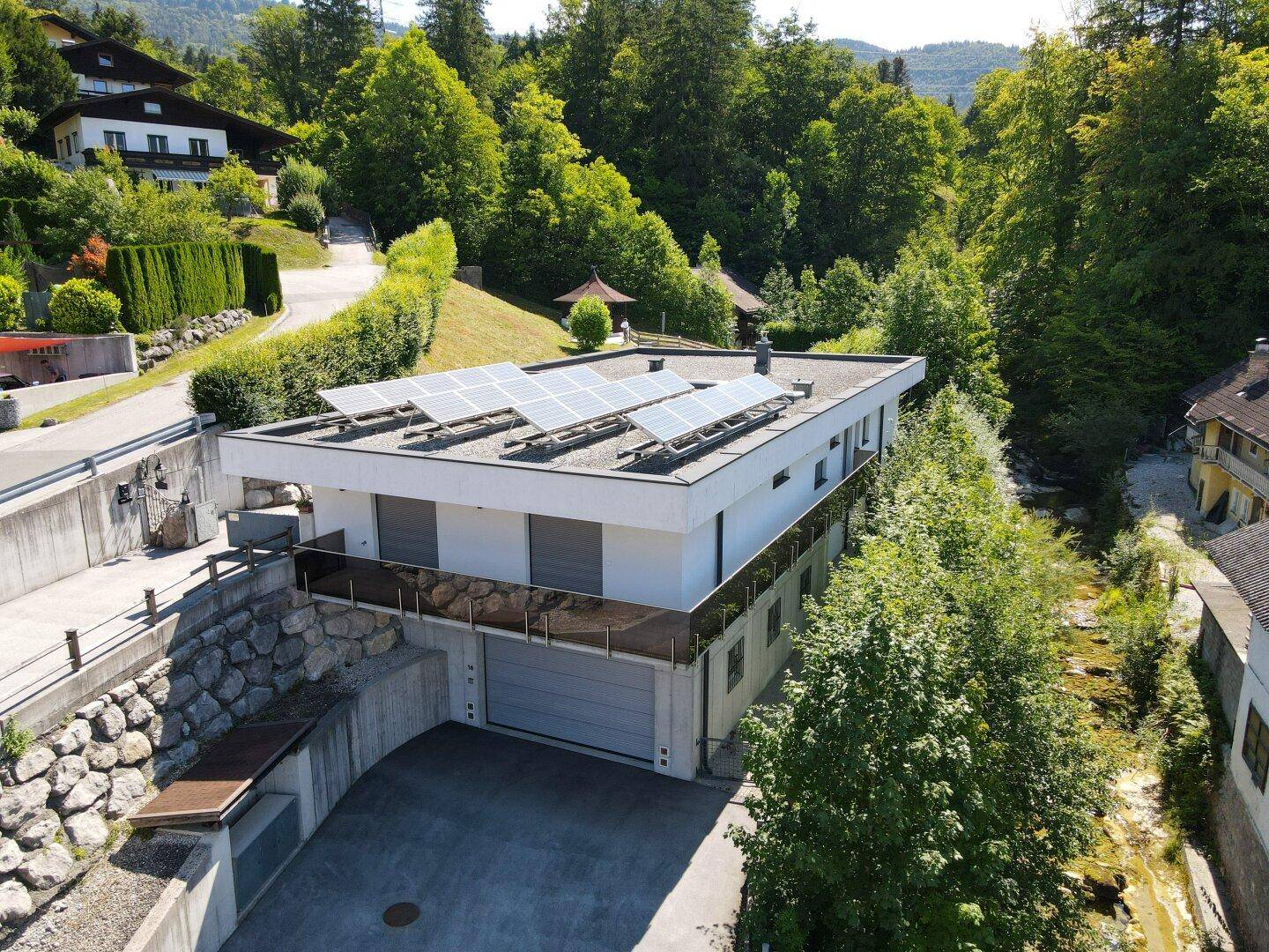 Seitenansicht des modernen Hauses mit integrierter Garage, Solaranlage auf dem Dach und üppiger Vegetation.