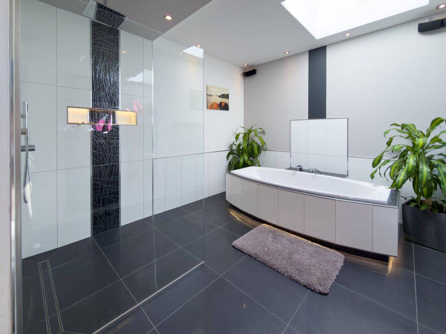 Geräumiges modernes Badezimmer mit dunklen Fliesen, großer Badewanne, begehbarer Dusche und Oberlicht.