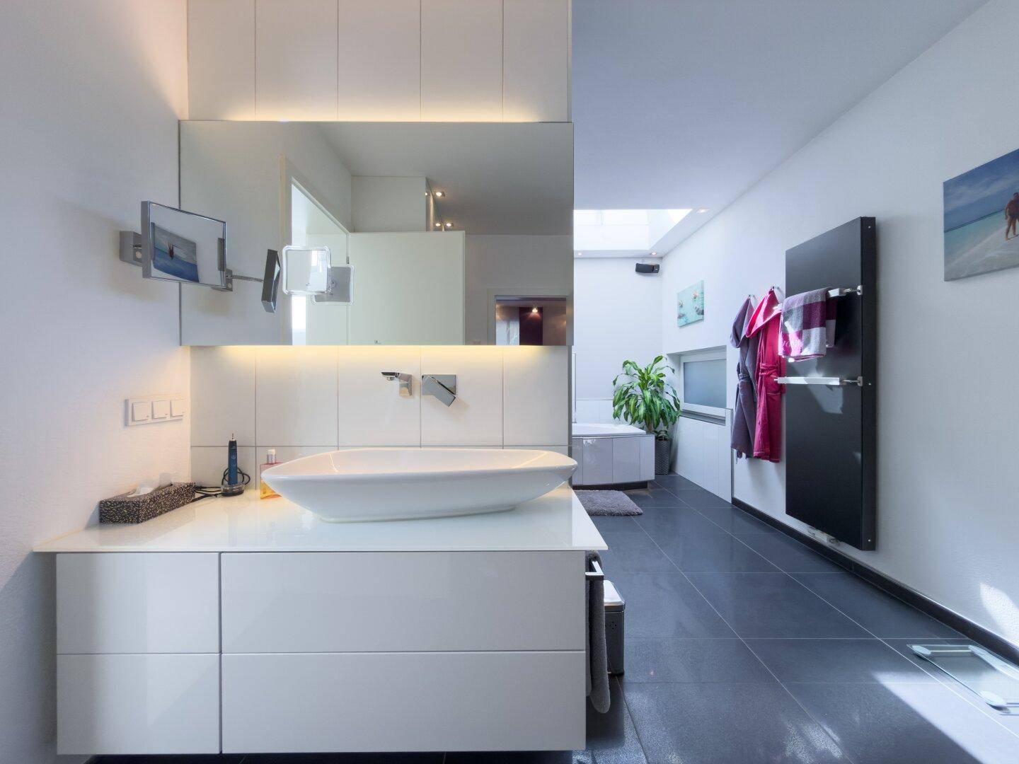 Elegantes Badezimmer mit modernem Waschtisch, großem Spiegel mit Beleuchtung und beheiztem Handtuchhalter.