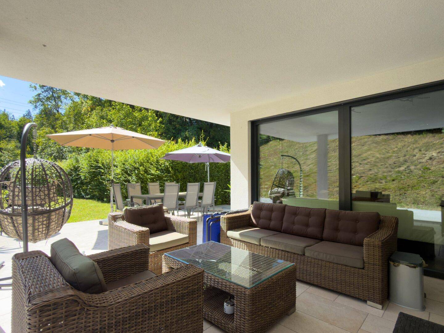 Gemütlicher Loungebereich auf der Terrasse mit Korbmöbeln und Blick in den Garten durch große Glasschiebetüren.