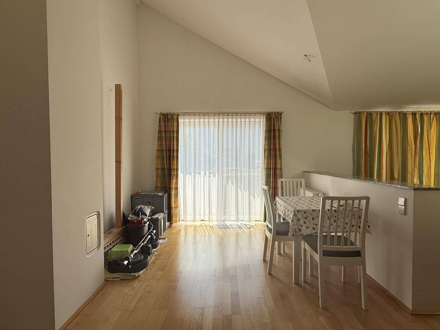 Heller Wohn- und Essbereich mit Holzboden, Dachschräge und Zugang zu einem Balkon.