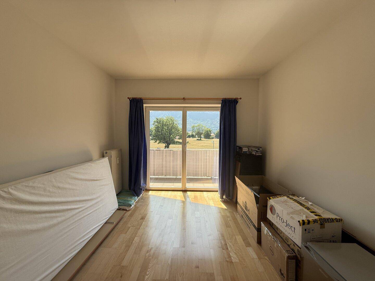 Helles Schlafzimmer mit Holzboden, Balkontür und schöner Aussicht auf die umliegende Natur.
