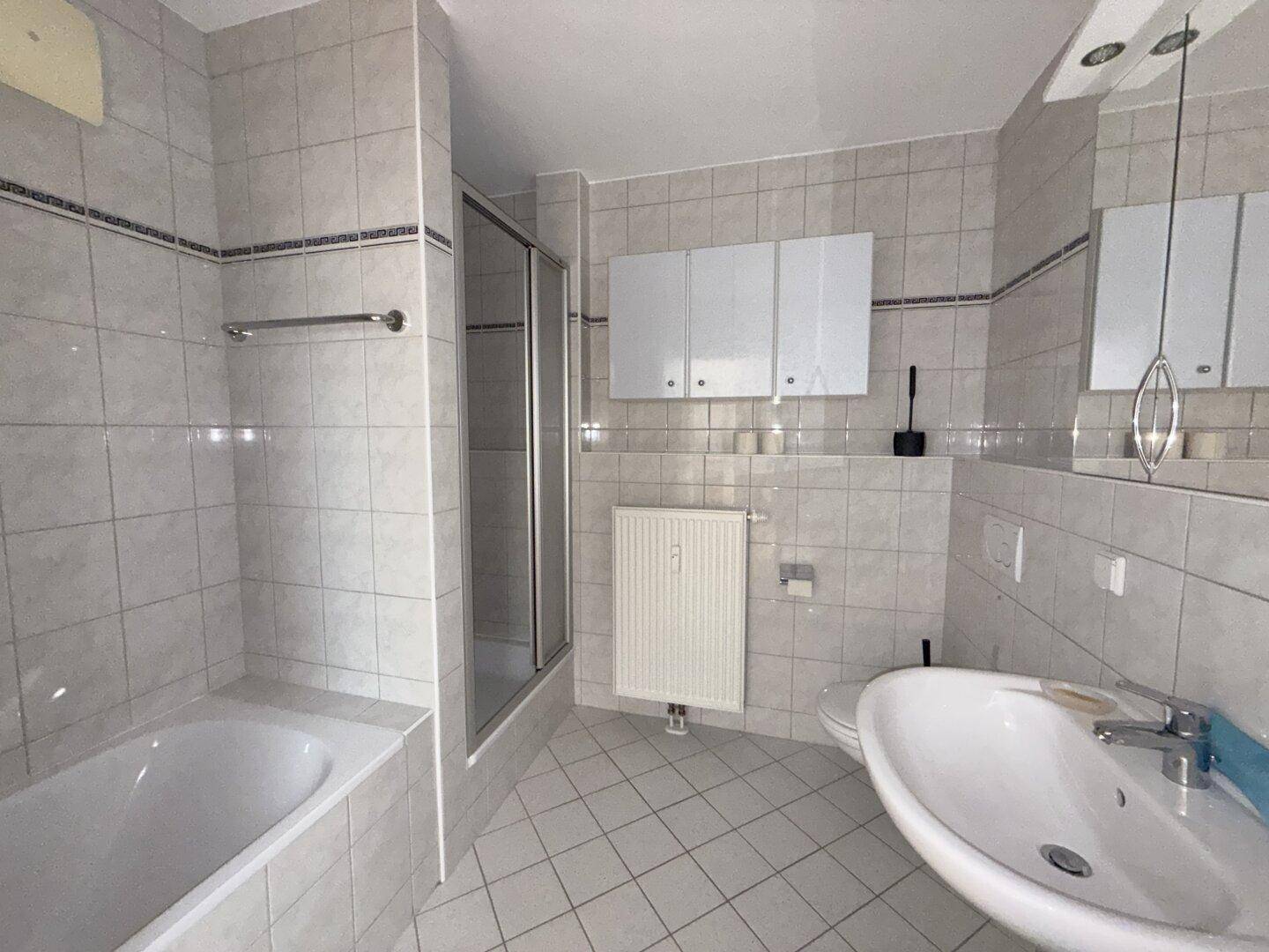 Modern gefliestes Badezimmer mit Badewanne, Duschkabine, Waschbecken und Heizkörper.