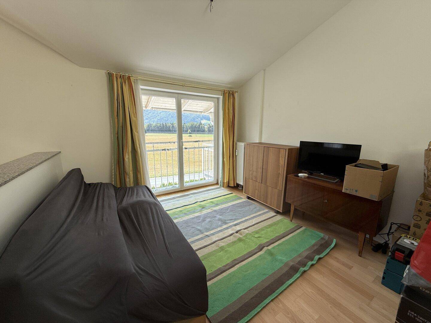 Gemütliches Schlafzimmer mit Teppich, Balkonzugang und weitem Blick auf die grüne Landschaft.