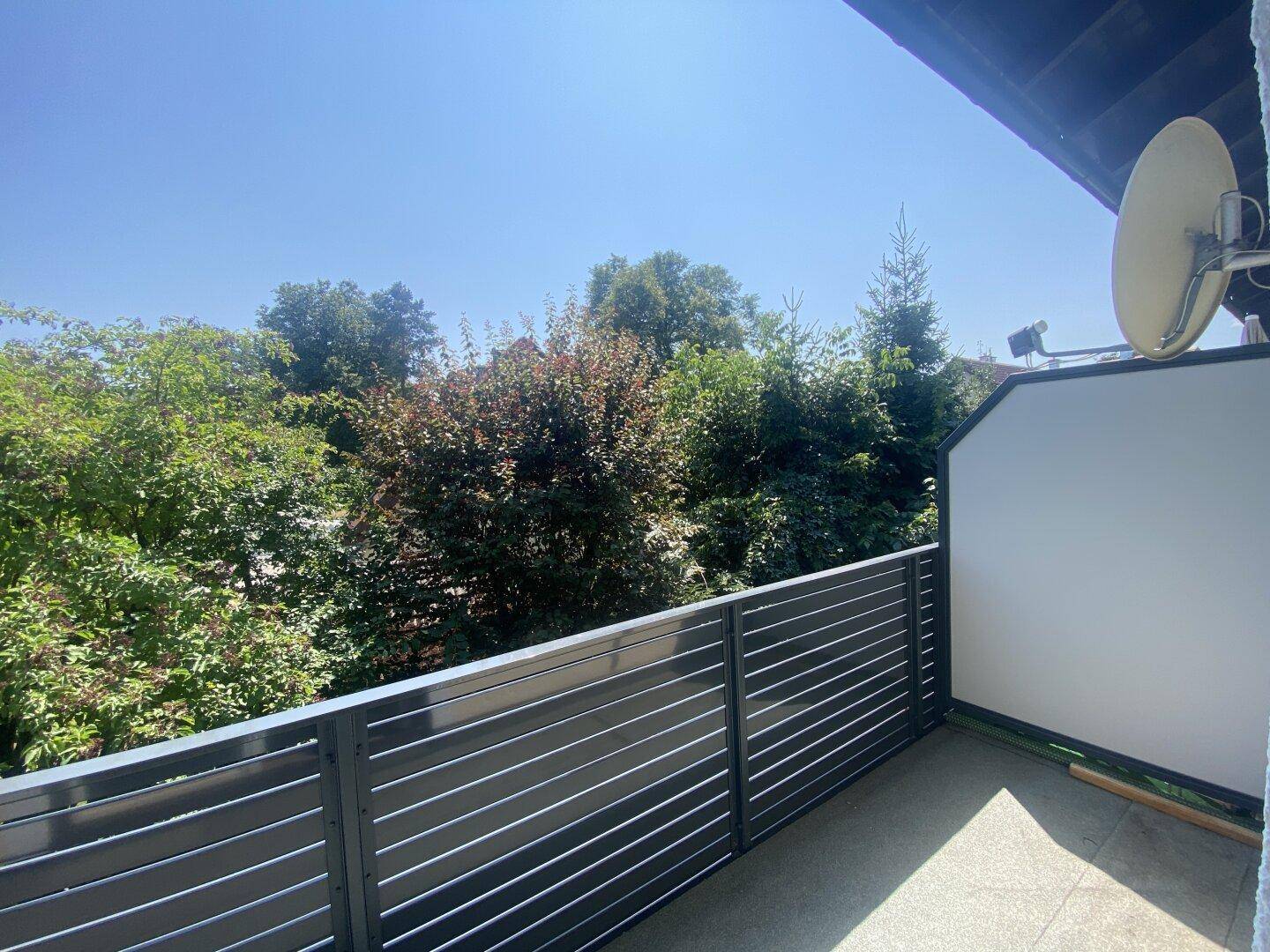 Sonniger Balkon mit Blick ins Grüne und moderner dunkler Brüstung.