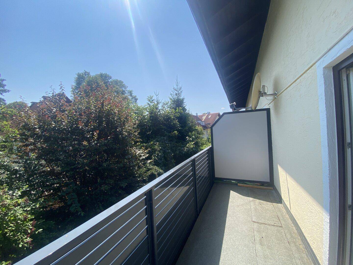 Balkon mit Fliesenboden und Satellitenschüssel, umgeben von viel Grün.